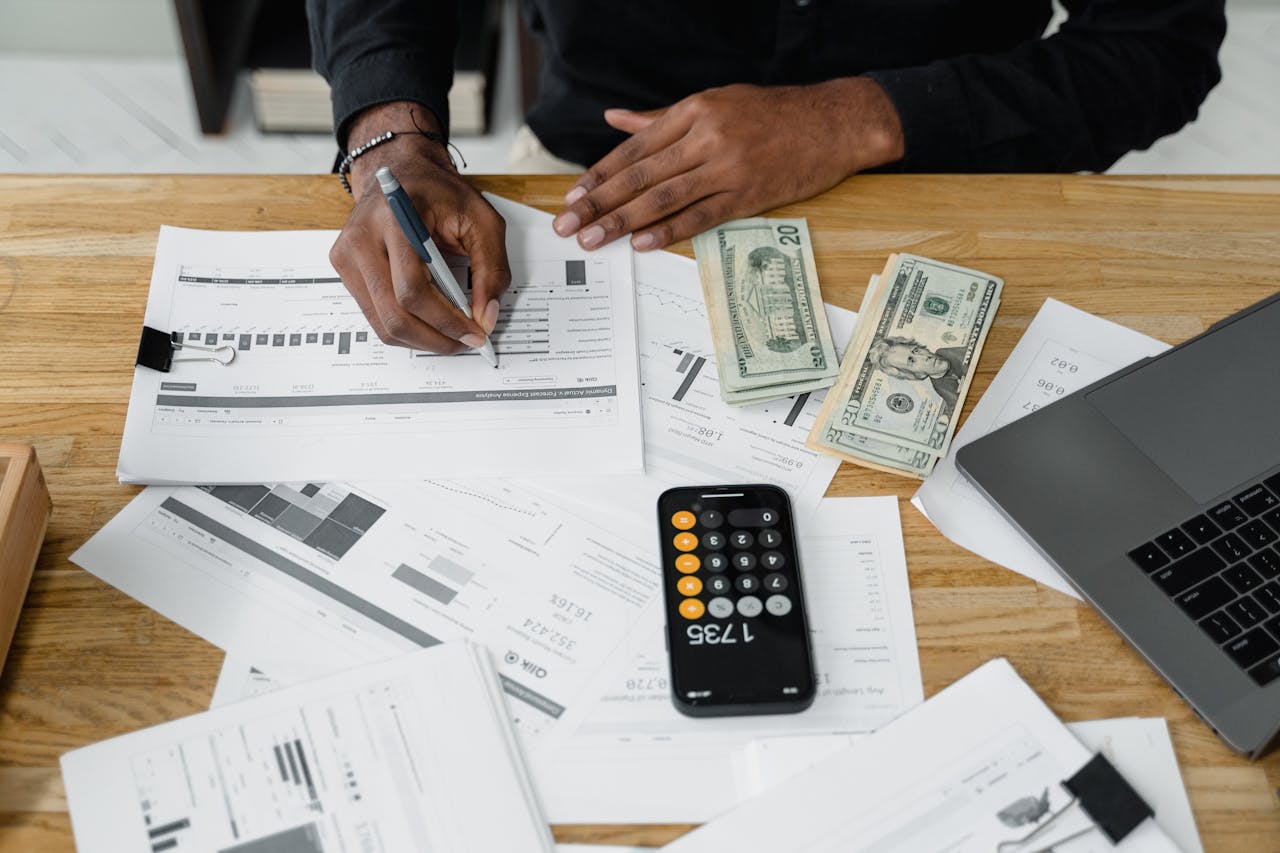 Man working on financial reports with calculator, money, and laptop on a desk.