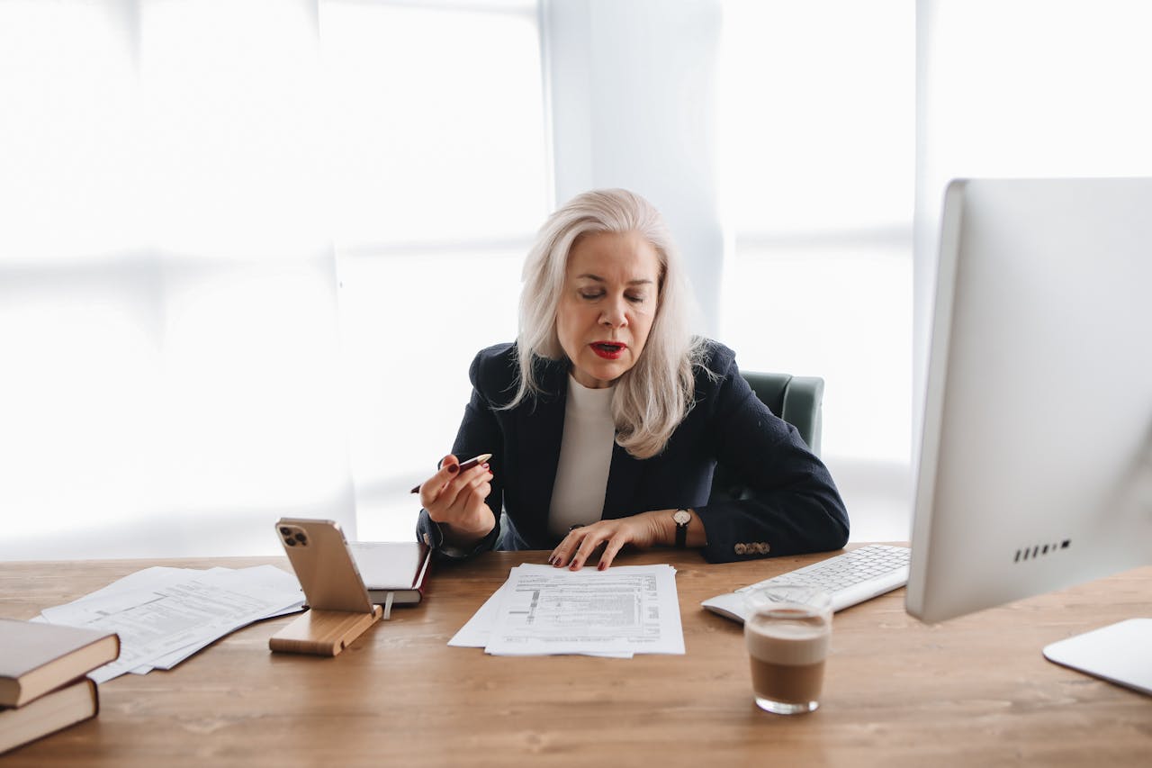 Senior woman in office reviewing financial documents with focused expression.